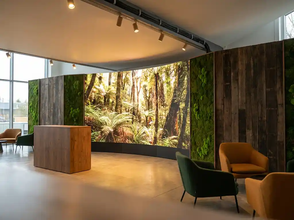 Messestand mit LED-Wand und Waldmotiv, lebenden Mooswänden, Holzakzenten und warmem Spotlicht auf Betonboden.